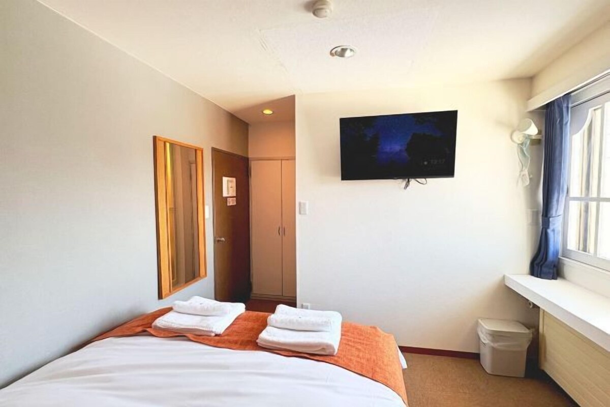 Una habitación de hotel con una cama, televisor, ventana y puerta.