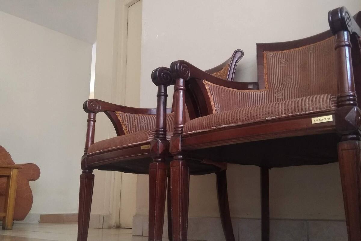 A wooden sofa with a cushion and a wooden chair in a room with tiled flooring and a clock on the wall.