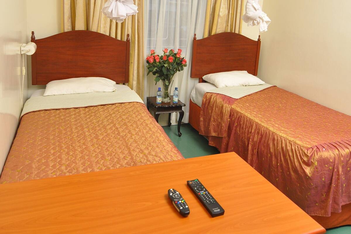 A hotel room with two single beds, a wooden table, a chair, and a nightstand with a vase of flowers.