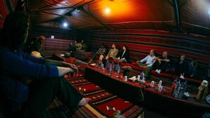 Un salón de conferencias con una larga mesa, alfombras rojas y un grupo de personas sentadas.