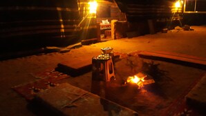 Un espacio exterior tenuemente iluminado con un brasero y una pequeña mesa, posiblemente un comedor, con un muro de piedra al fondo.