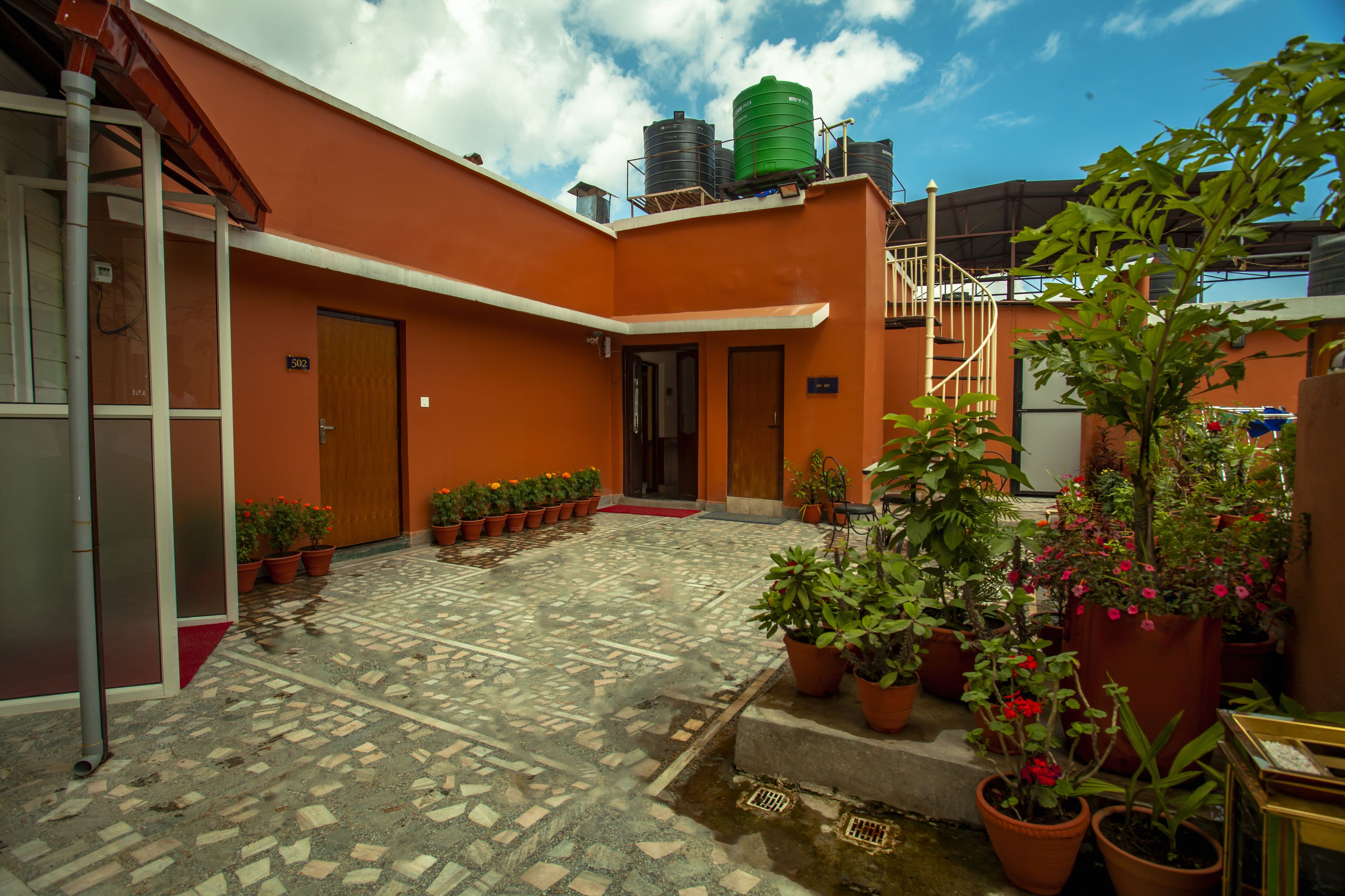 Un patio con plantas en macetas, suelo de baldosas y una escalera que sube a un nivel superior.
