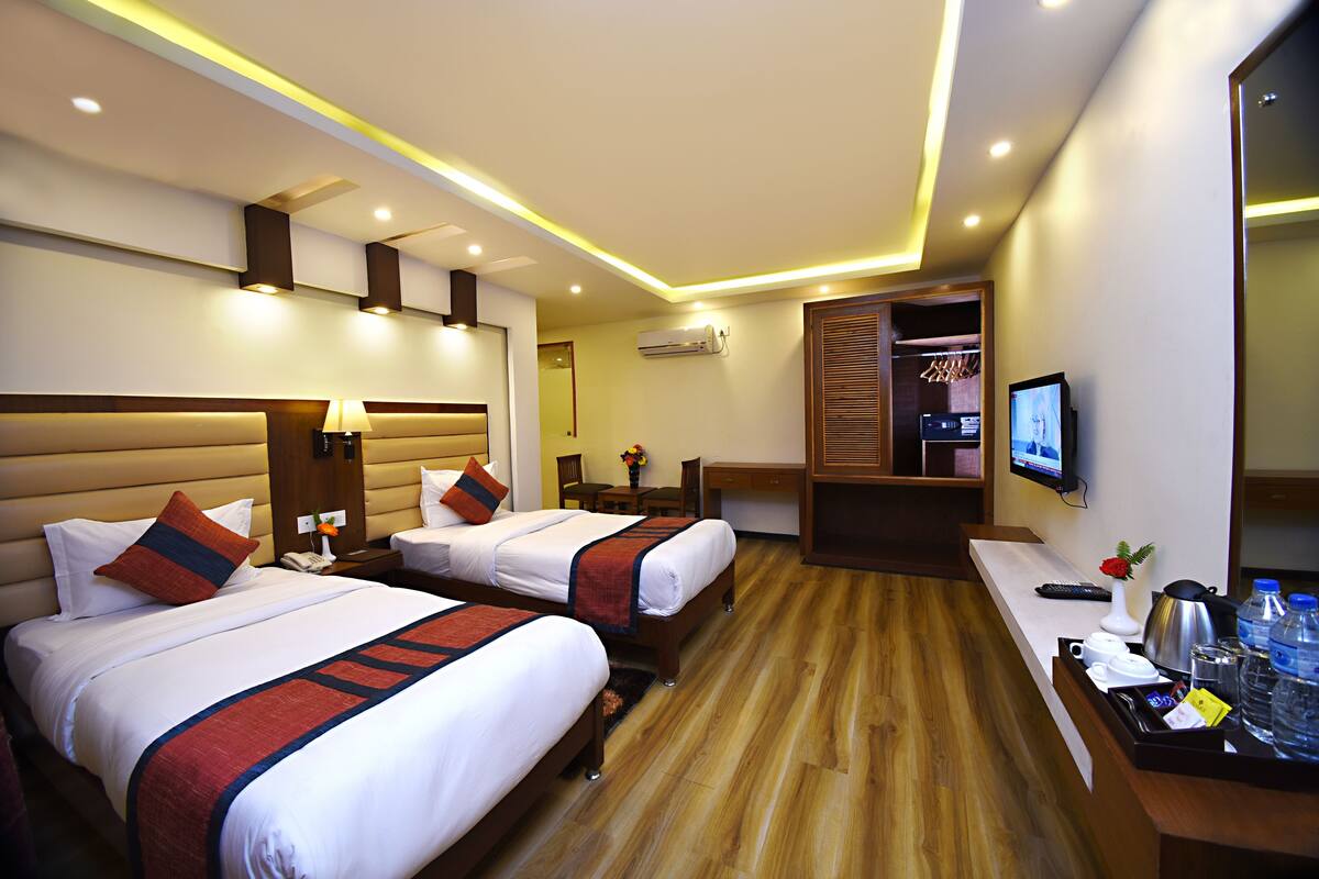 A hotel room with two beds, a desk, a TV, and a bathroom visible through a door.