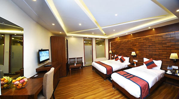 Une chambre d’hôtel avec deux lits, un bureau avec une télévision, un panier de fruits et un plancher en bois.
