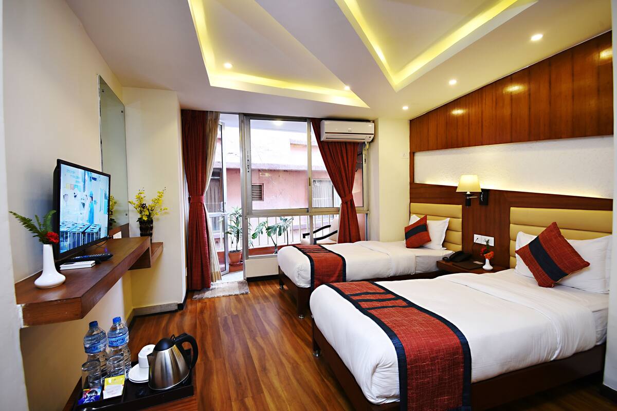 A hotel room with two beds, a TV, a desk with a computer, a coffee maker, and a window with curtains.