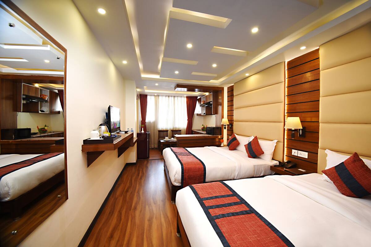 A hotel room with two beds, a desk, a mirror, a vanity, and a bathroom.