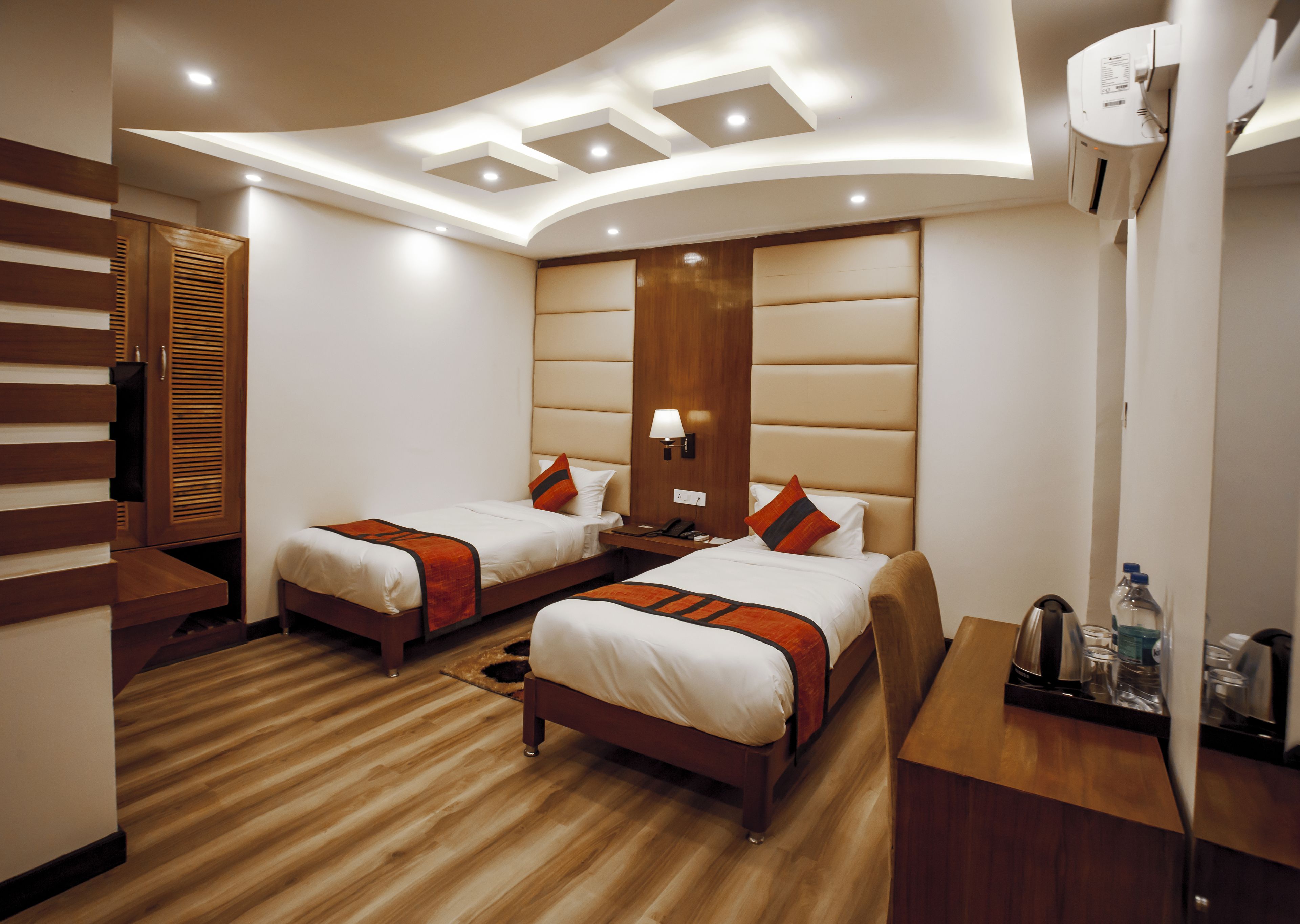 Une chambre d’hôtel avec deux lits, une armoire en bois, un bureau avec une lampe et un distributeur d’eau.