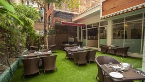 An outdoor patio area with wicker furniture and green artificial grass, surrounded by brick walls and plants. - Hotel Jampa (Kathmandu)