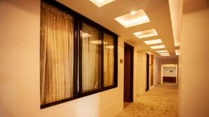 A hotel hallway with a carpeted floor, large windows with curtains, and recessed ceiling lights. - Hotel Jampa (Kathmandu)