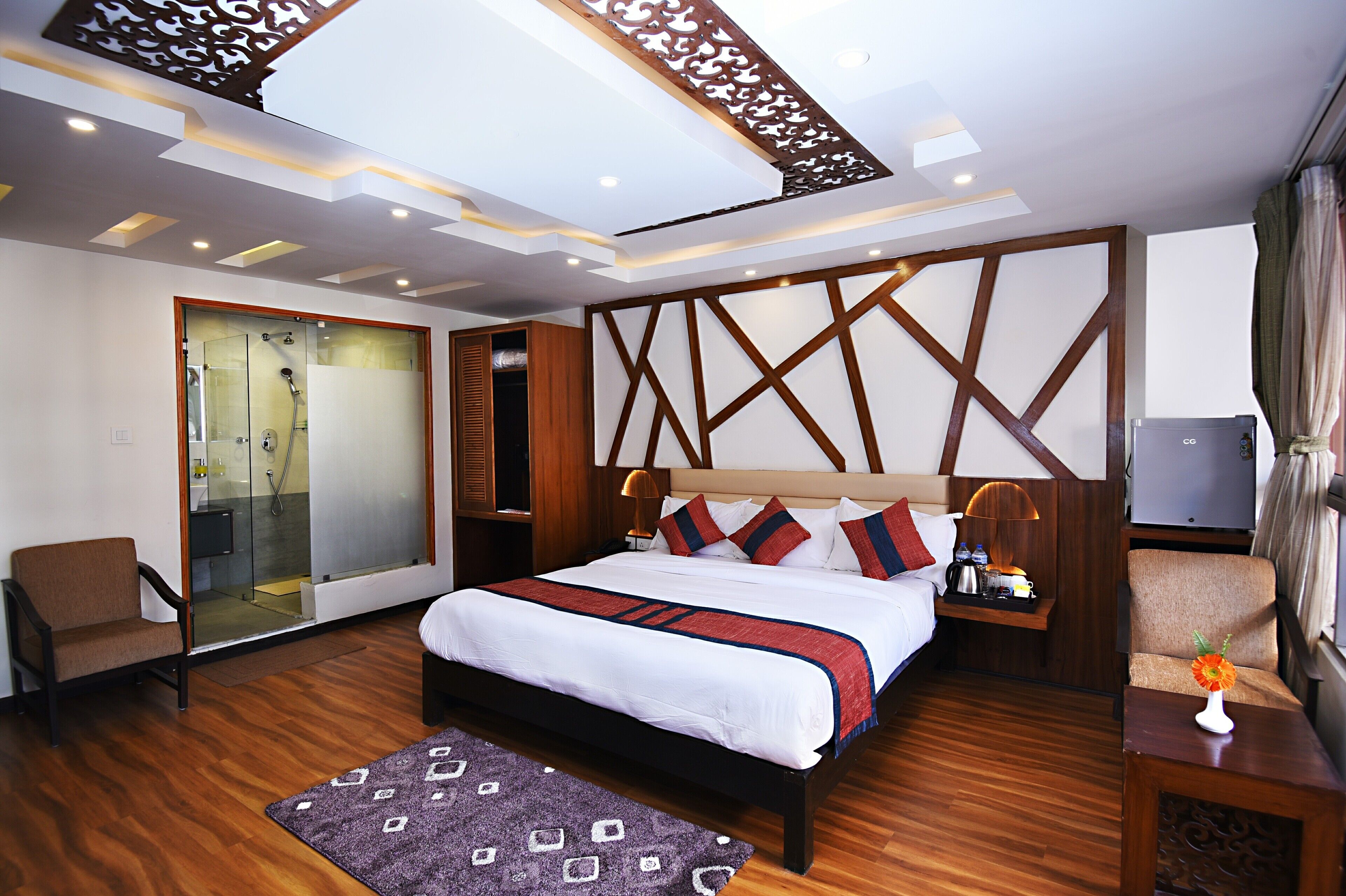 A modern hotel room with a large bed, a seating area, a shower room, and a TV.