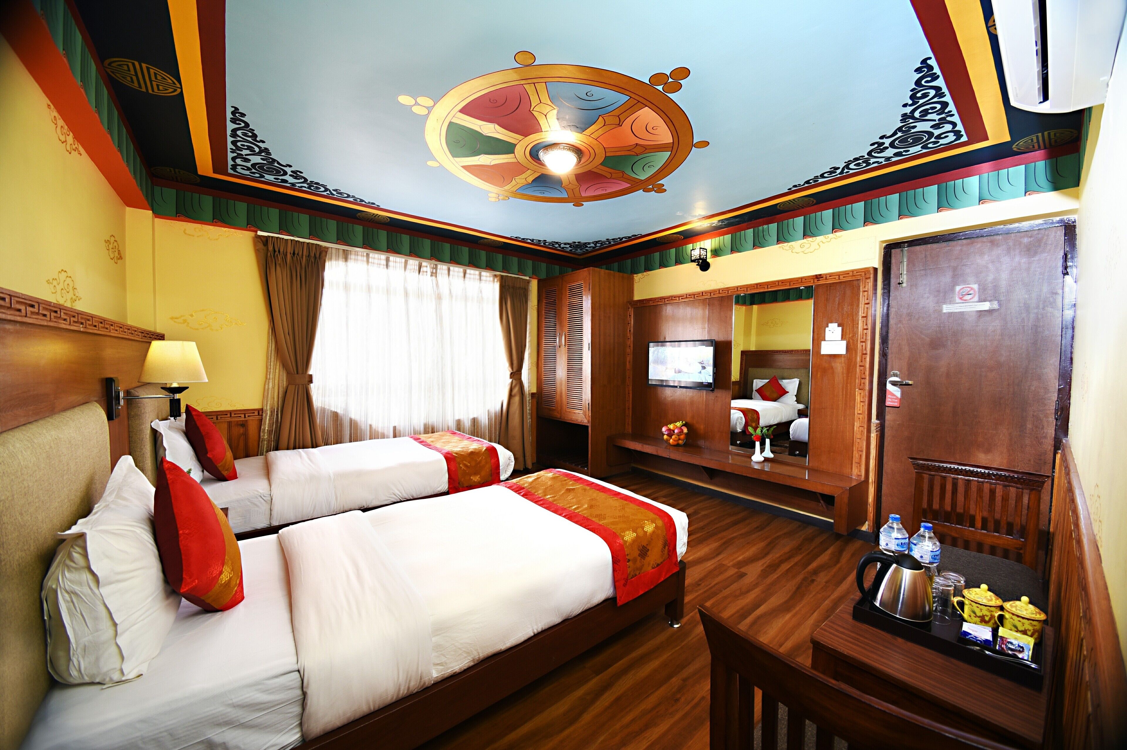 A hotel room with two beds, a television, a desk with a kettle, and a mirror.