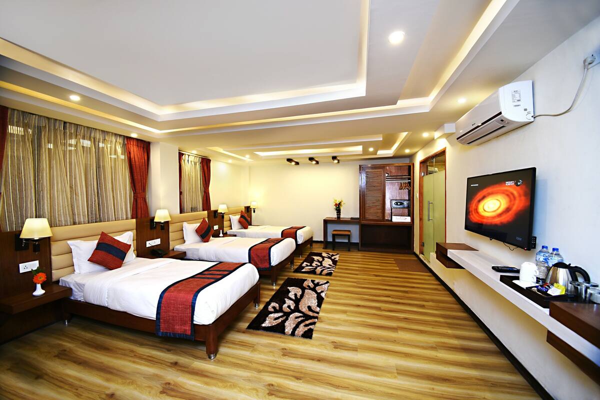 A hotel room with two beds, a TV, a desk, and an air conditioning unit.