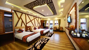 A hotel room with two beds, a wooden floor, a TV, a desk with a coffee machine, and a balcony with a view. - Hotel Jampa (Kathmandu)