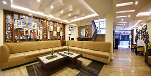 A modern lobby with a large beige sofa, two glass-top coffee tables with decorative items, a wooden partition with mirrors, and a staircase leading to another area. - Hotel Jampa (Kathmandu)