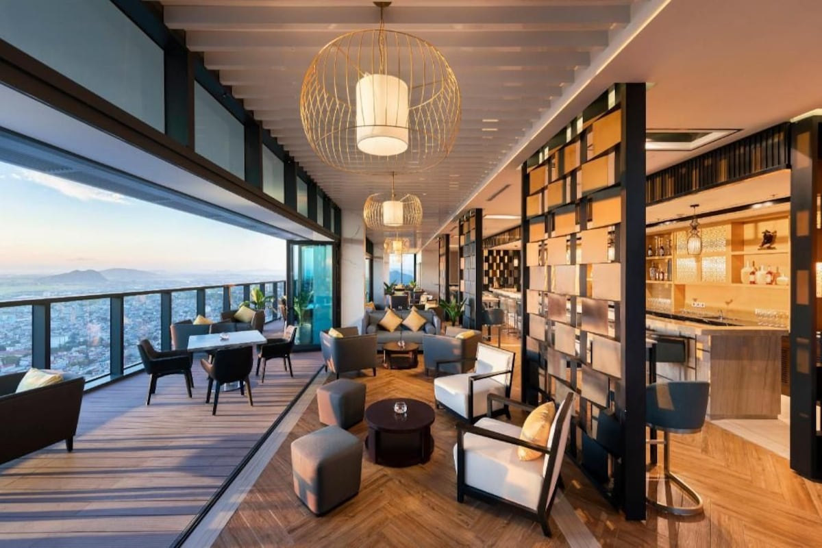A modern interior with a high ceiling, a bar area with shelves, and a seating area with a view.