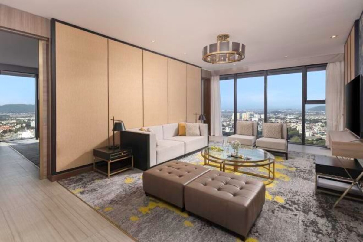 Una sala de estar moderna con sofá, reposapiés y sillones, una mesa de centro y un ventanal con vistas a la ciudad.