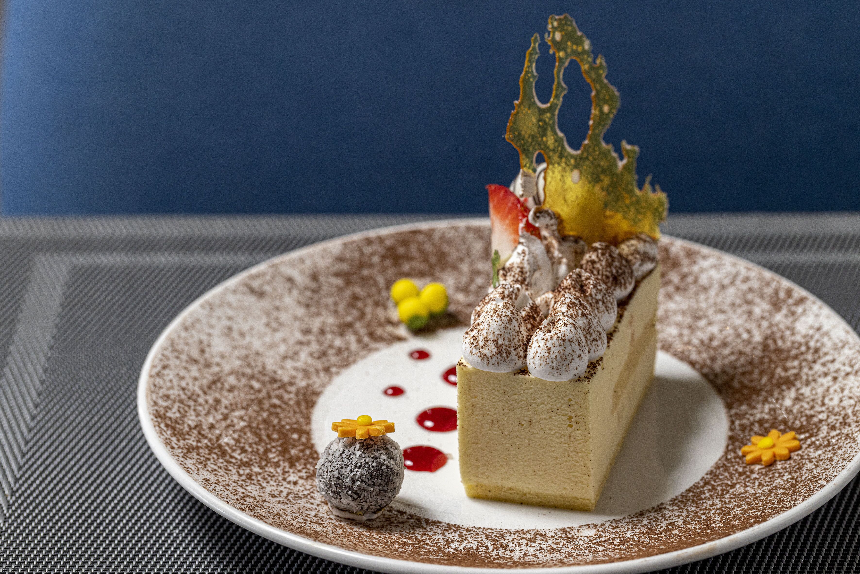 Un dessert présenté sur une assiette, agrémenté d’une feuille décorative et d’une petite sphère.