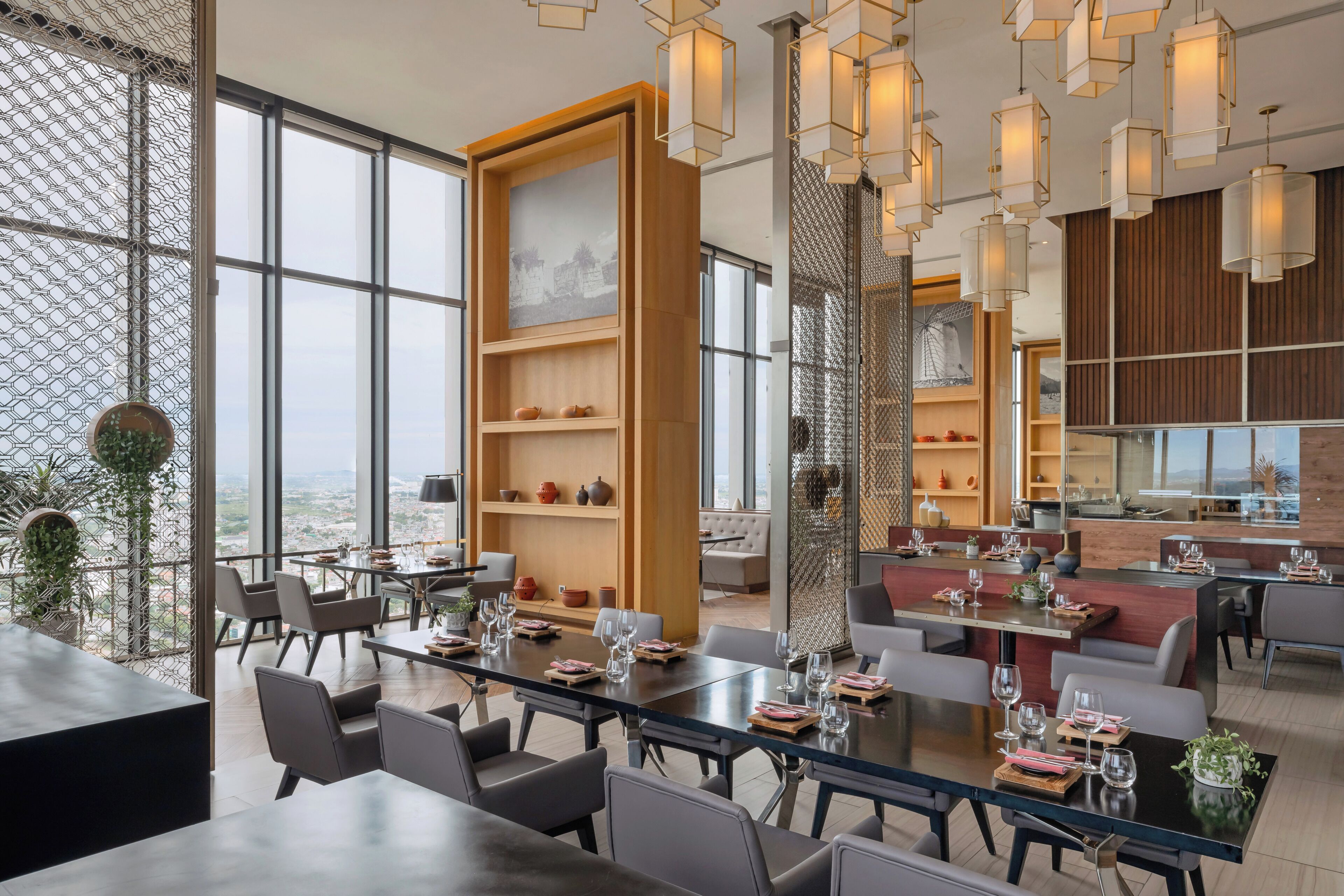A modern hotel dining area with multiple tables, chairs, and a large window offering a city view.