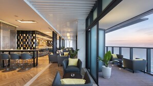 A modern lounge area with seating, a bar, and large windows overlooking the sea. - Meliá Vinpearl Thanh Hoa (Hac Thanh)