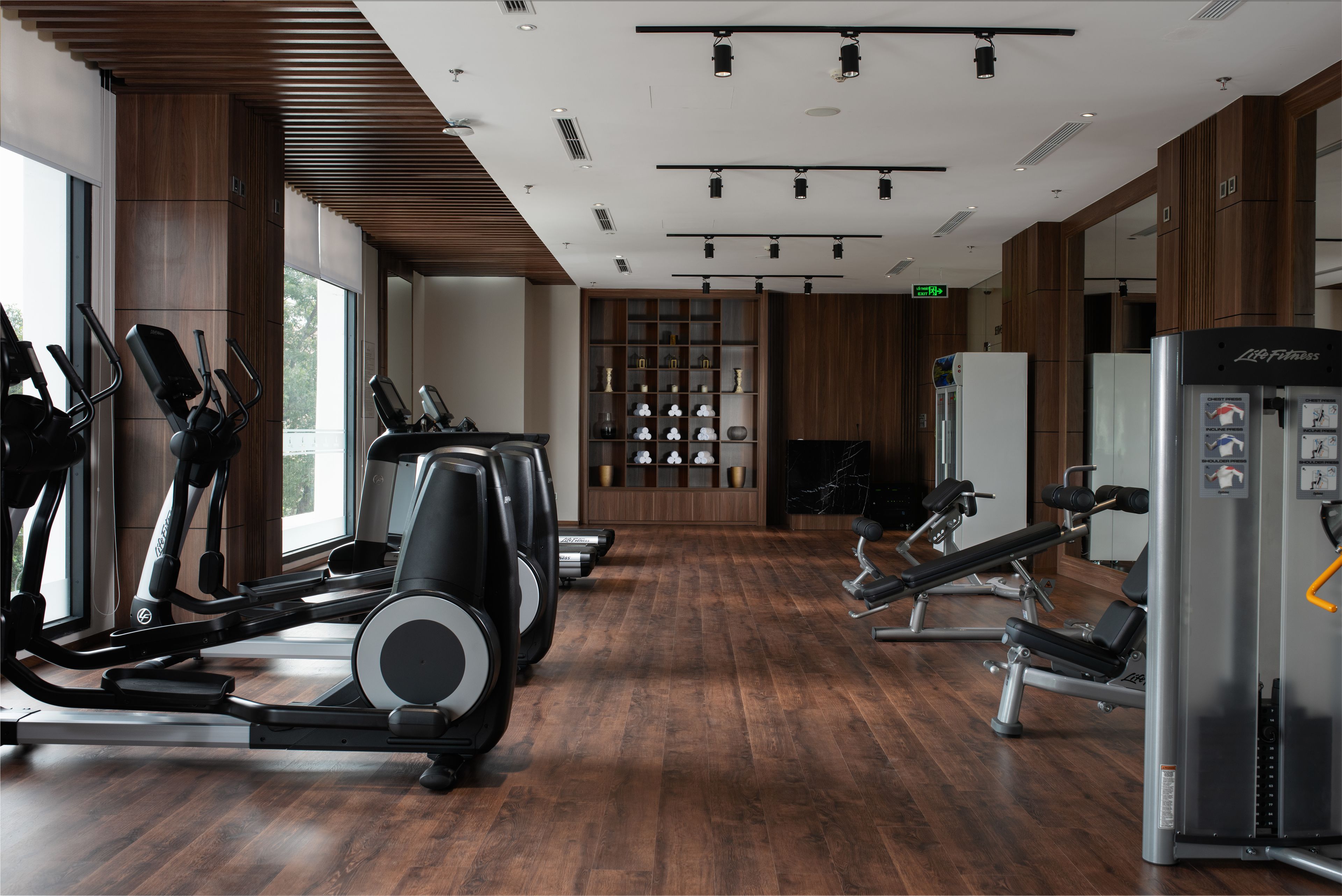 A gym with exercise equipment, wooden floors, and large windows.