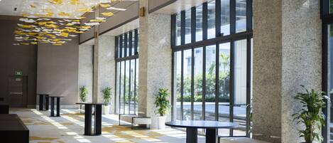Een ruime lobby met grote ramen, modern meubilair en hangende decoraties.
