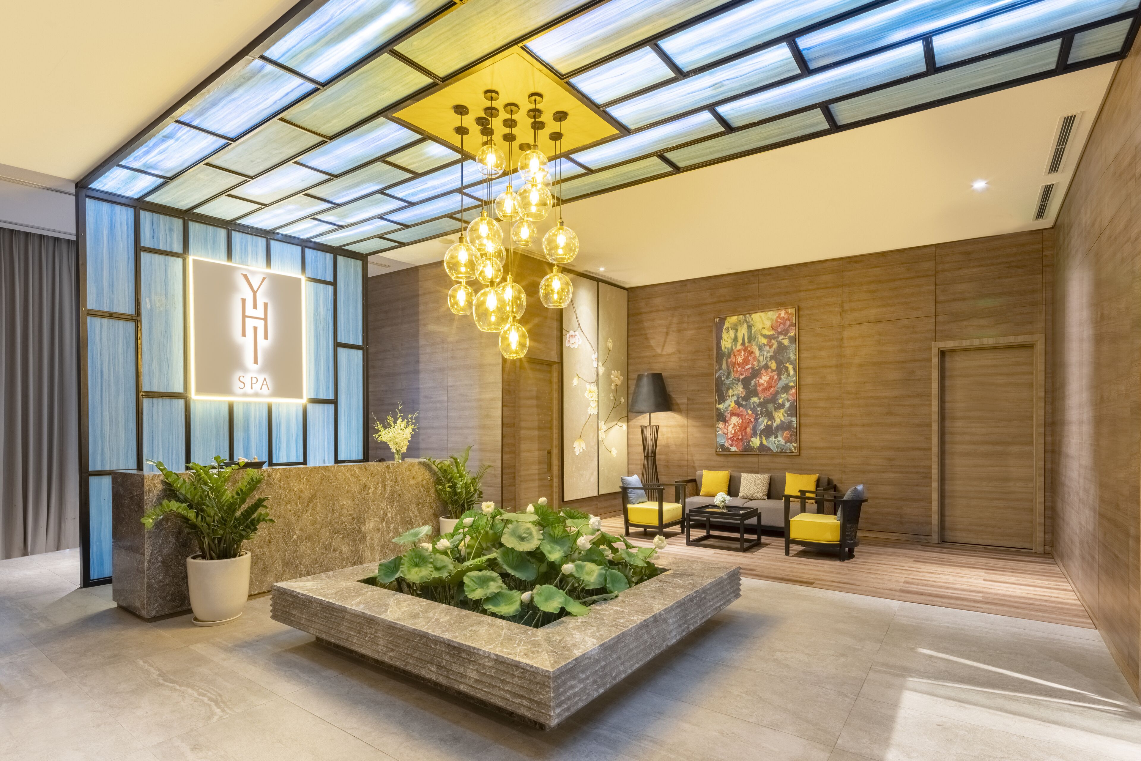 A modern spa interior with a reception desk, a hanging light fixture, a water feature, and a seating area.