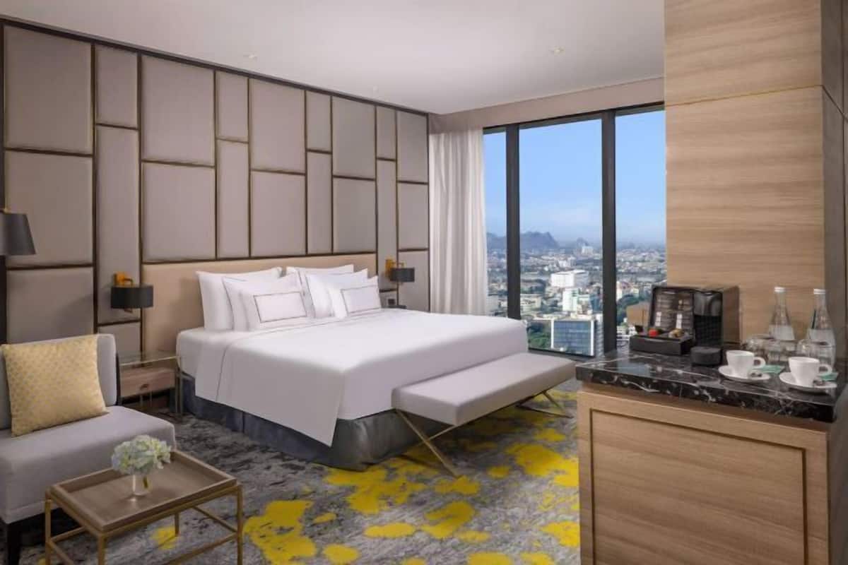 A hotel room with a large bed, a sofa, a small table, and a view of the city.