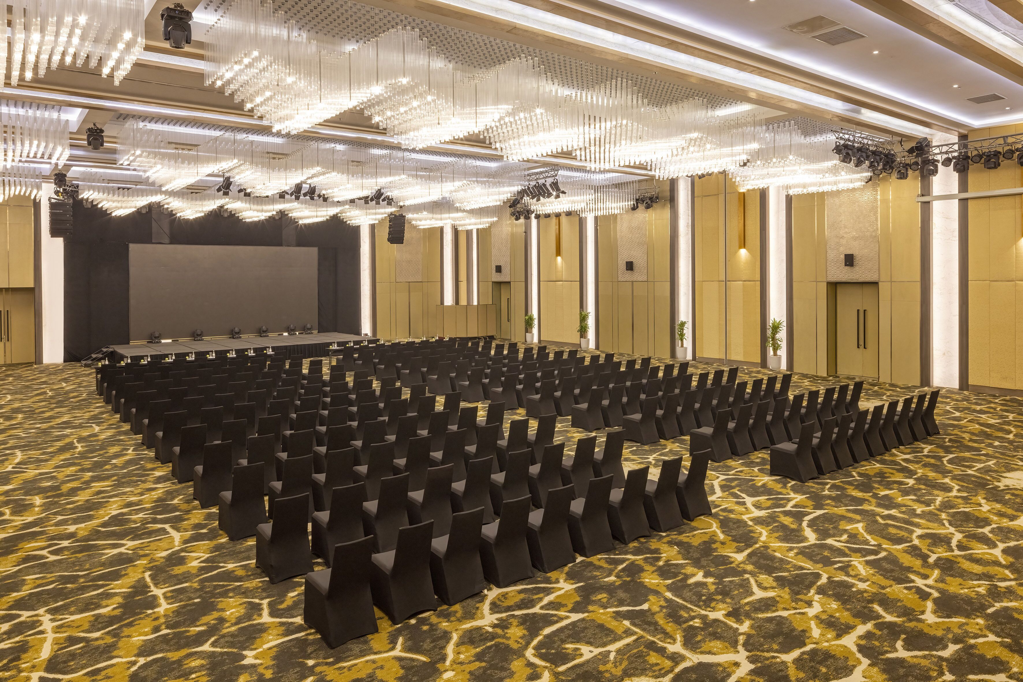 A large conference room with rows of black chairs, a stage, and a patterned carpet.