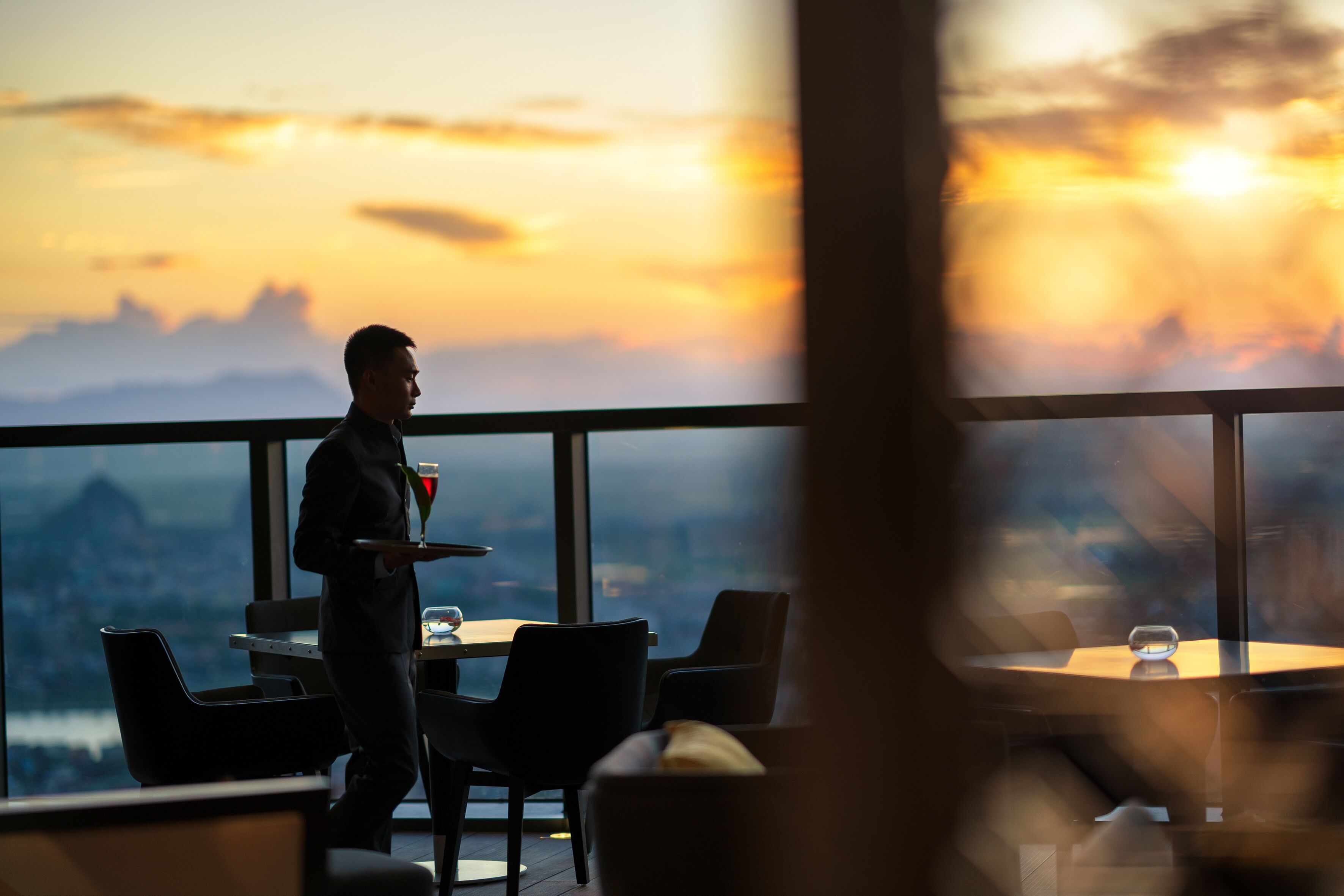 Un restaurante con vista a un atardecer sobre un paisaje urbano.