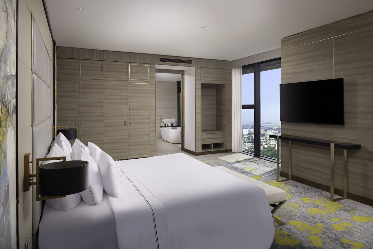 A modern hotel room with a large bed, a flat-screen TV, and a city view.
