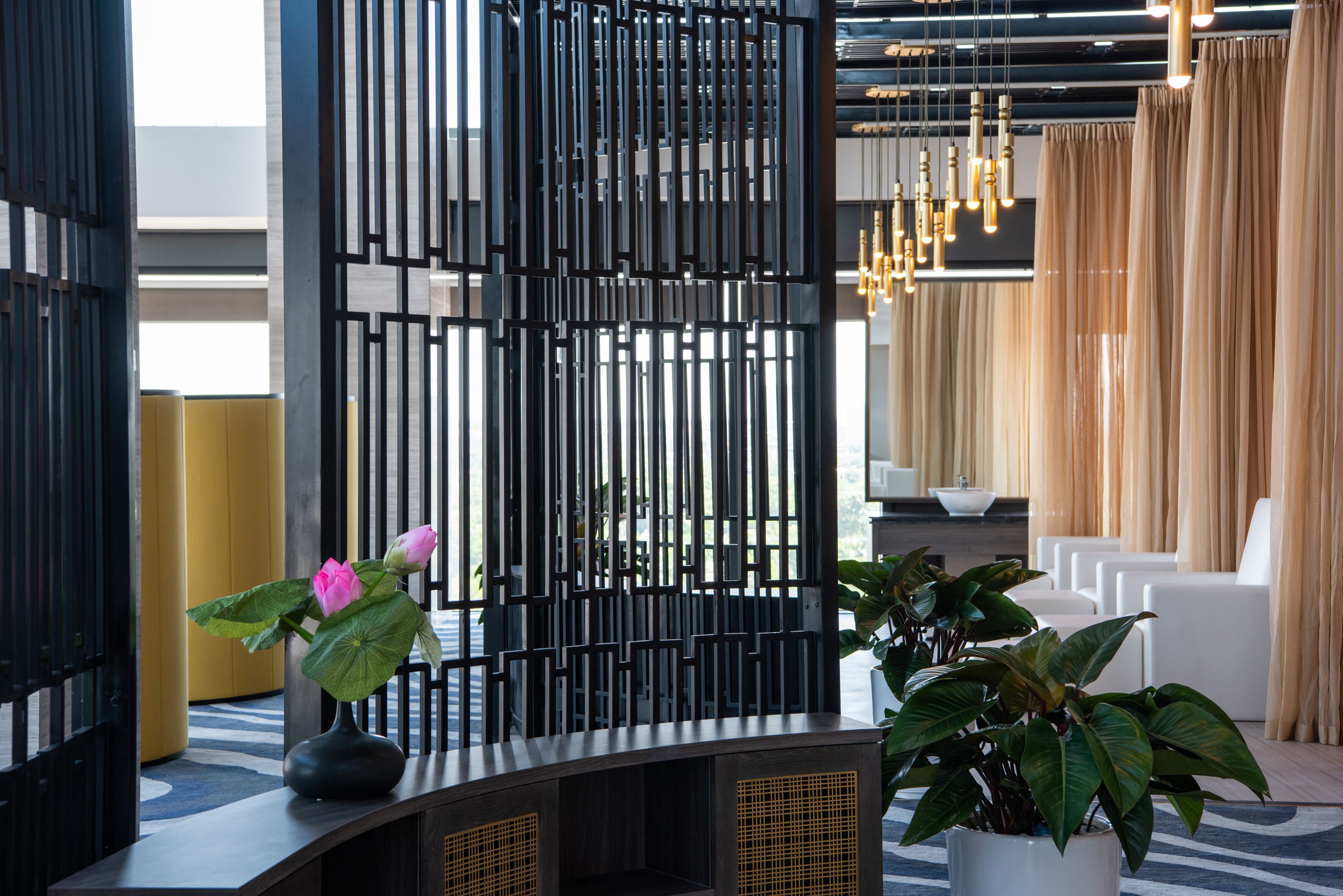 A modern reception area with a decorative black partition, a vase with a pink flower, and a potted plant.