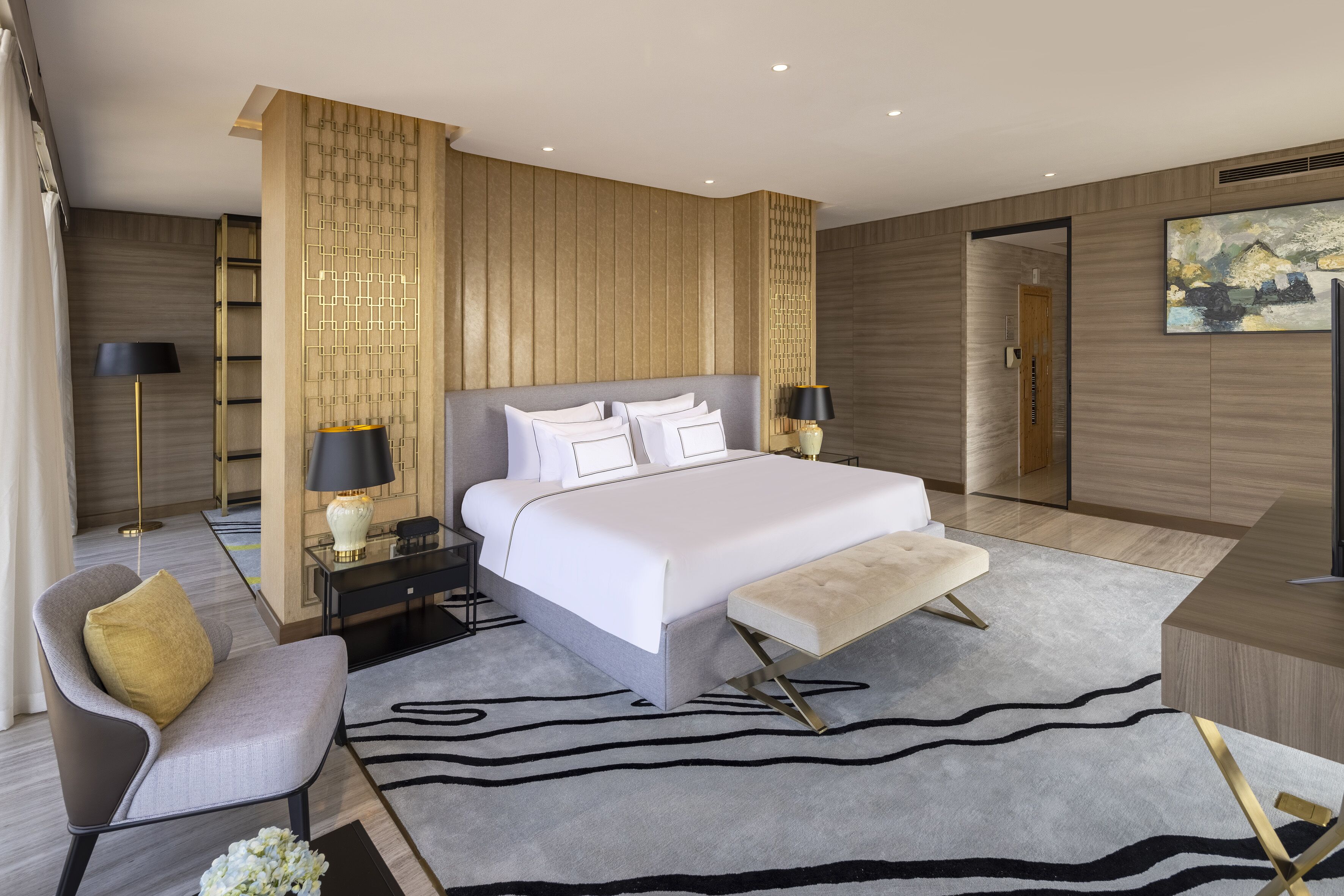 A modern hotel room with a large bed, a desk, a chair, and a nightstand with lamps.