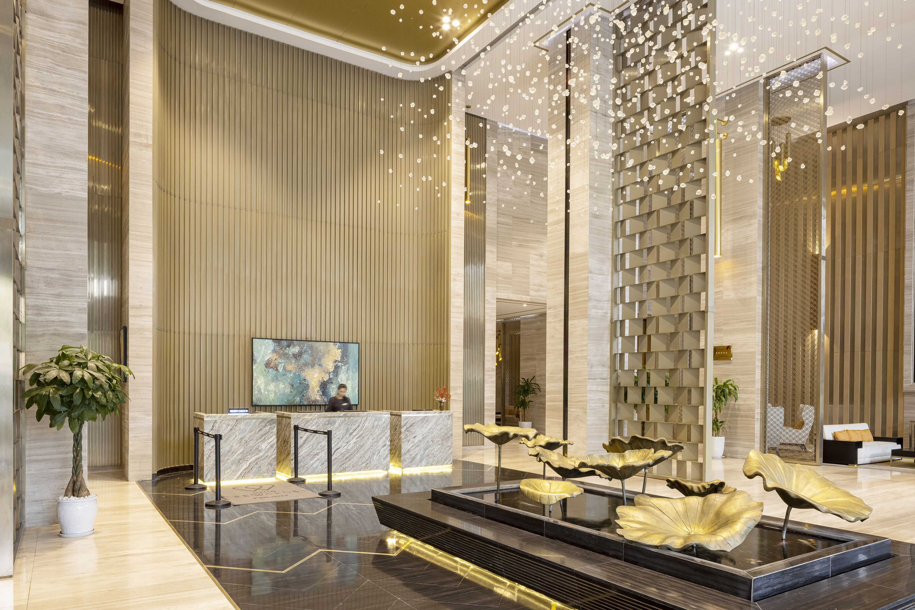 A modern lobby with a reception desk, a large abstract painting, a water feature, and a seating area.