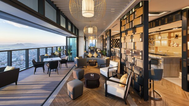 A modern lounge area with a panoramic city view, a bar, and a seating arrangement with sofas and chairs. - Meliá Vinpearl Thanh Hoa (Hac Thanh)