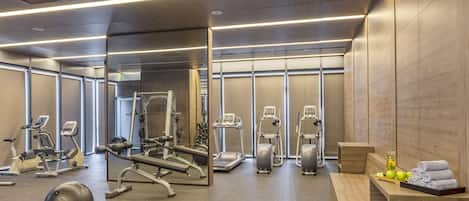 Un gimnasio moderno con diferentes equipos de ejercicio, una banca y una mesa con toallas y manzanas.