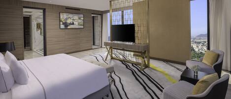 A modern hotel room with a large bed, a TV on a wooden stand, a sofa, and a view of the city.