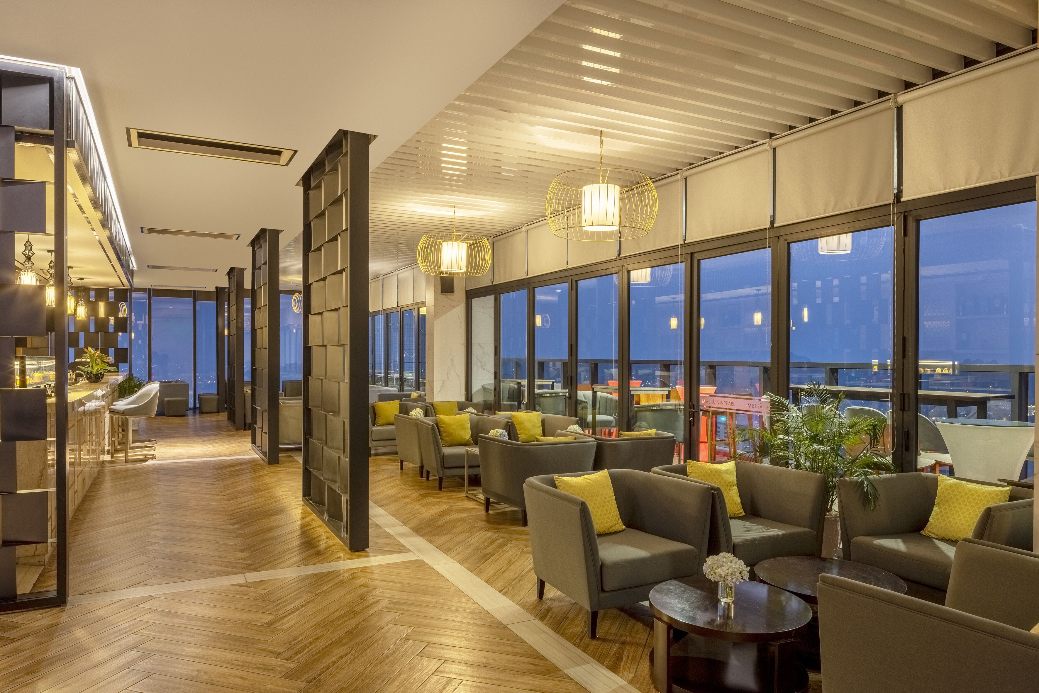 Un moderno vestíbulo de hotel con suelo de madera, zonas de estar, ventanas amplias y vistas a la ciudad.