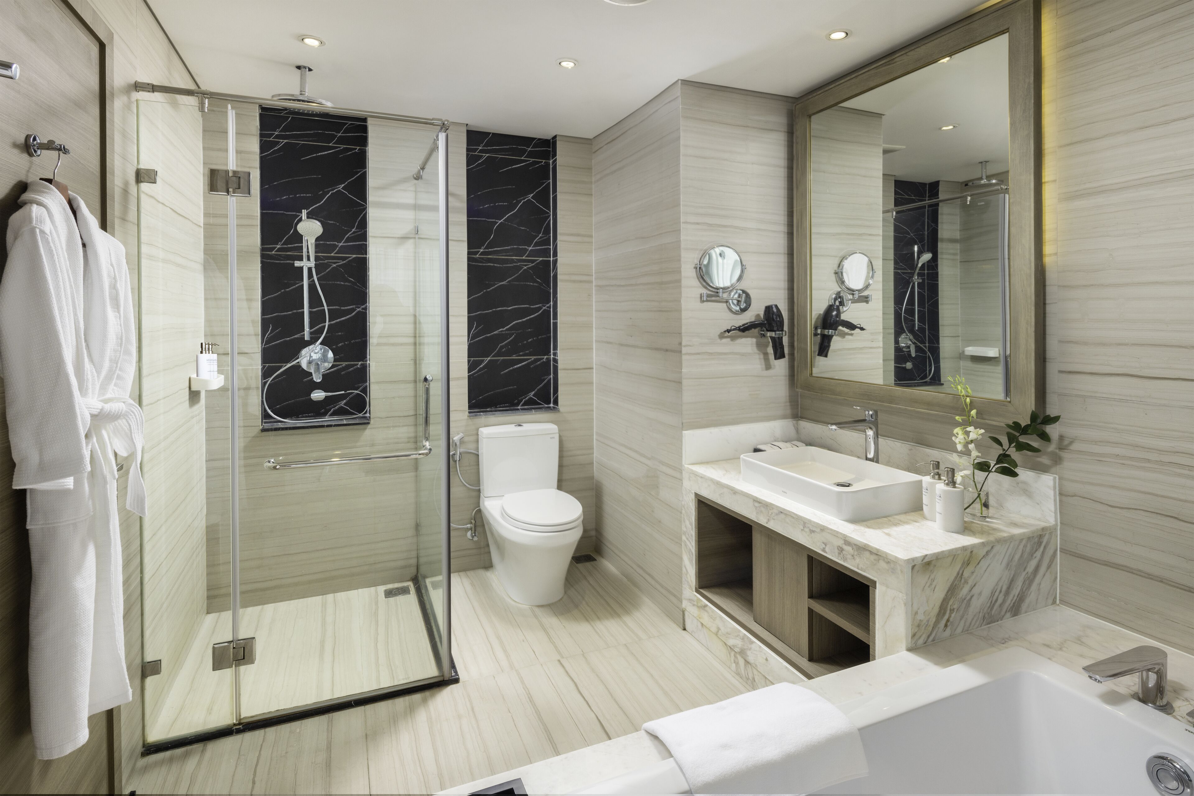 Un baño moderno con ducha acristalada, inodoro, lavamanos y un espejo grande.