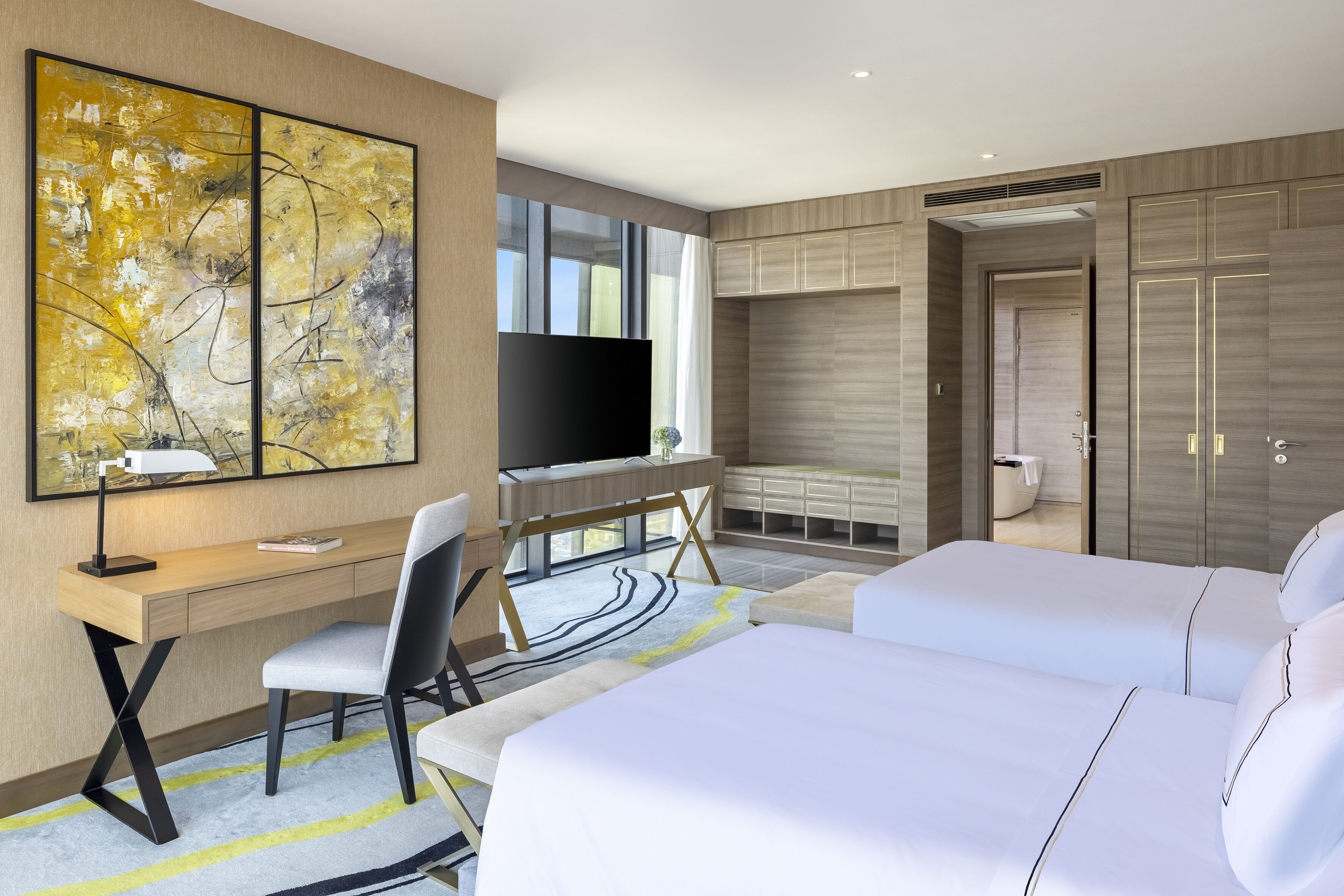 A modern hotel room with a desk, two beds, a TV, and a large abstract painting.