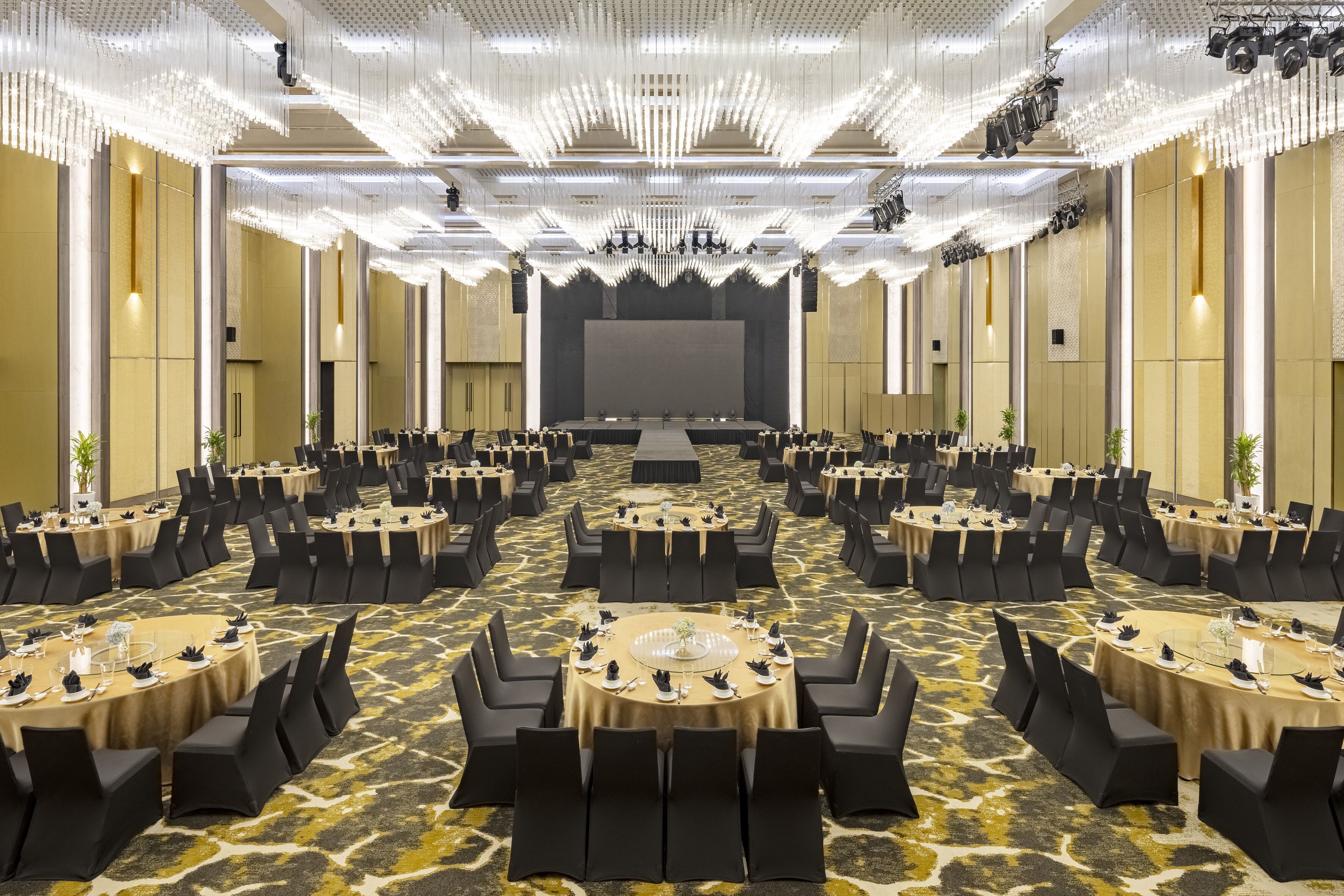 Une grande salle de conférence avec des tables rondes, des chaises noires et une scène à l’avant.