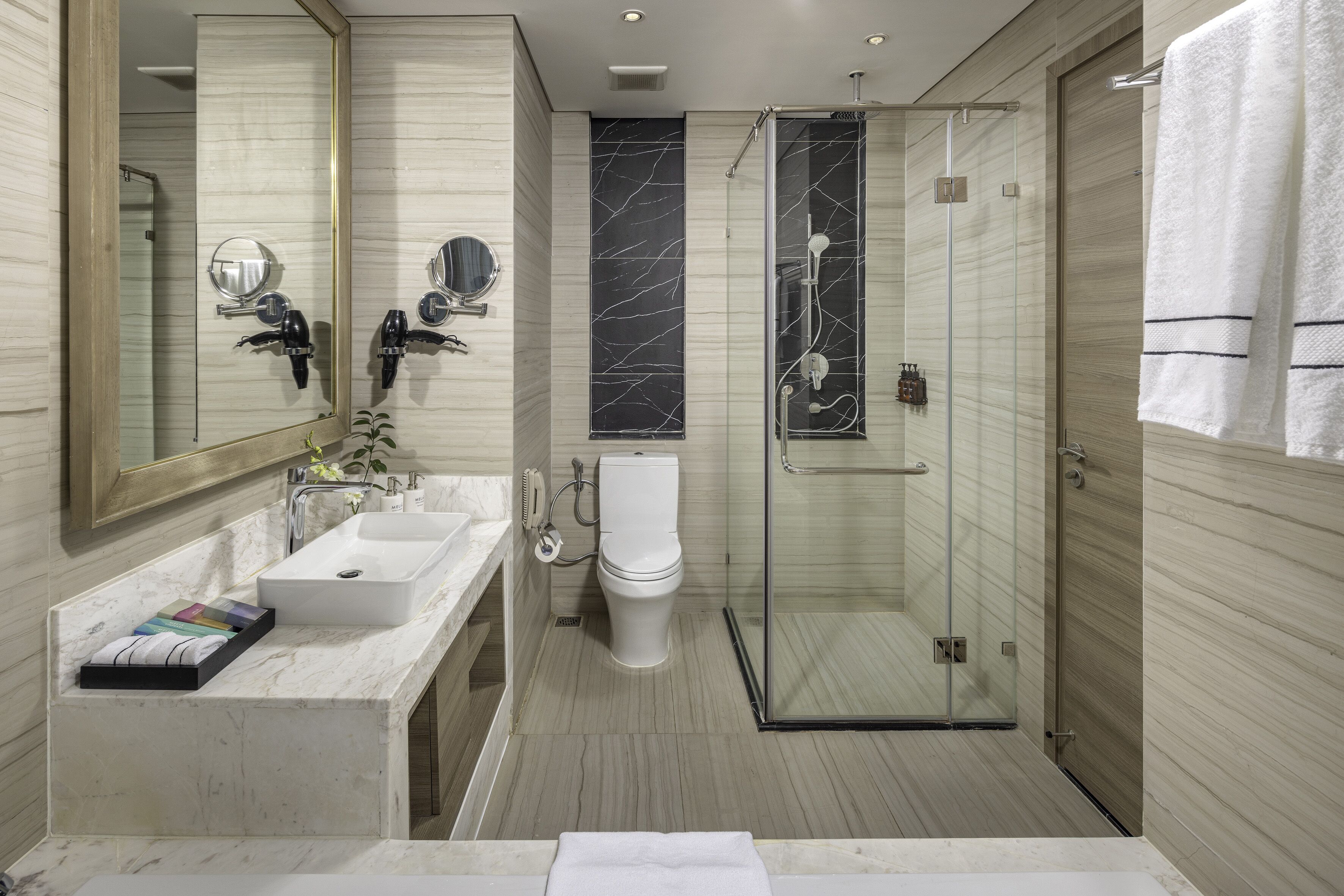 A modern bathroom with a large mirror, a white sink, a toilet, and a glass-enclosed shower.