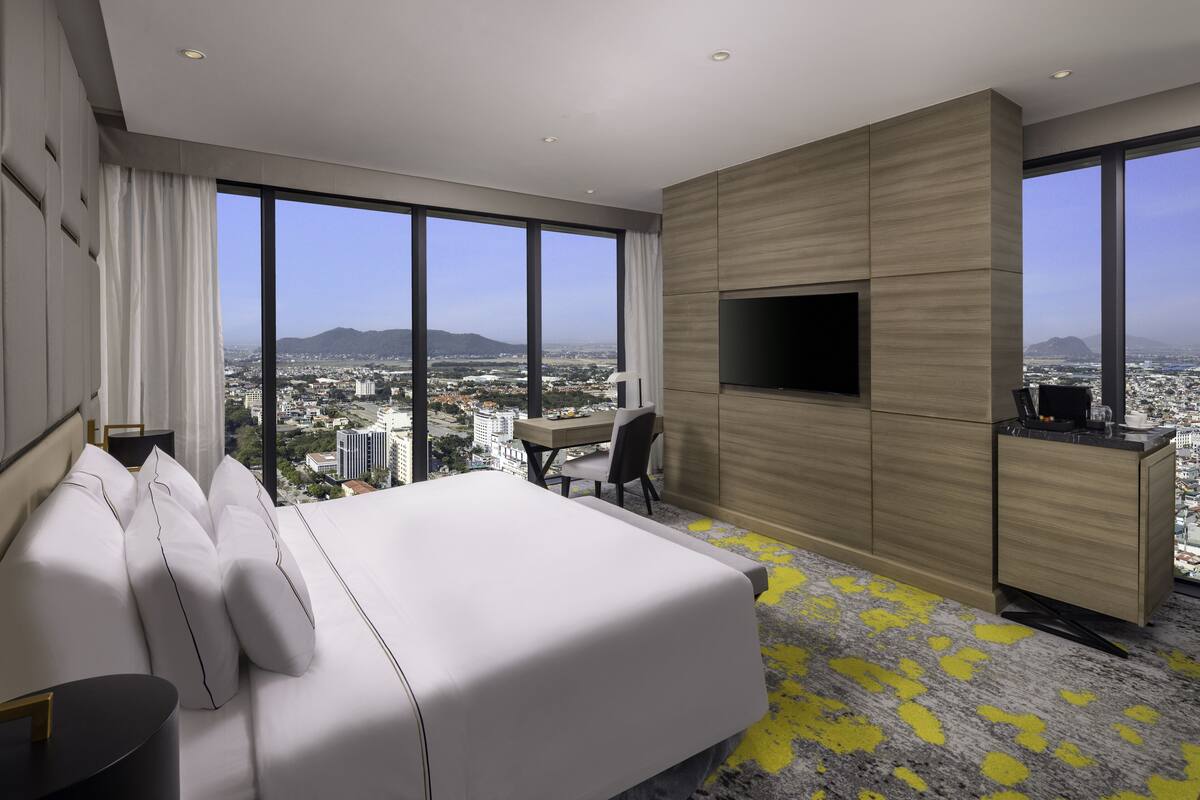 A modern hotel room with a large bed, a desk, a TV, and a city view.
