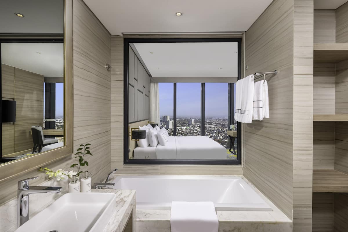 A modern bathroom with a large bathtub, a mirror, and a view of a cityscape through a large window.