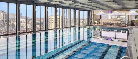 A rooftop swimming pool with clear views of the cityscape, large windows, and sun umbrellas.