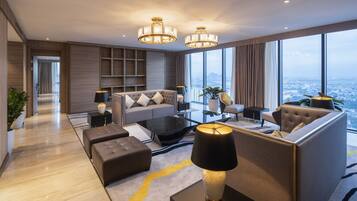 A modern hotel living room with a sofa, ottoman, coffee table, and a view of the city through large windows.