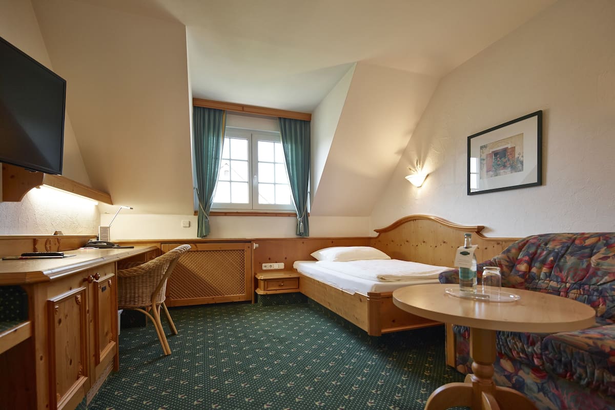 Quarto de hotel com cama, escrivaninha, cadeira, mesinha, televisão e janela com cortinas.
