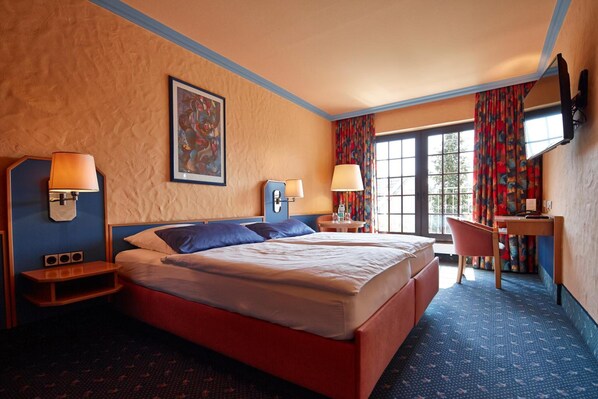 Habitación de hotel con una cama grande, dos mesitas de noche, un escritorio, una silla y una ventana con cortinas.