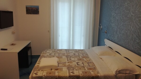 Un dormitorio con cama, escritorio, televisor y ventana con cortinas.