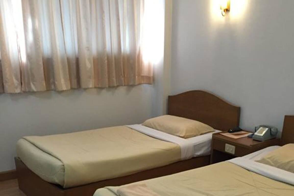 Een hotelkamer met twee enkele bedden, houten hoofdeinden, een nachtkastje met een lamp en een raam met gordijnen.