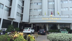 Um hotel de vários andares com entrada central, algumas bandeiras e um estacionamento com carros.